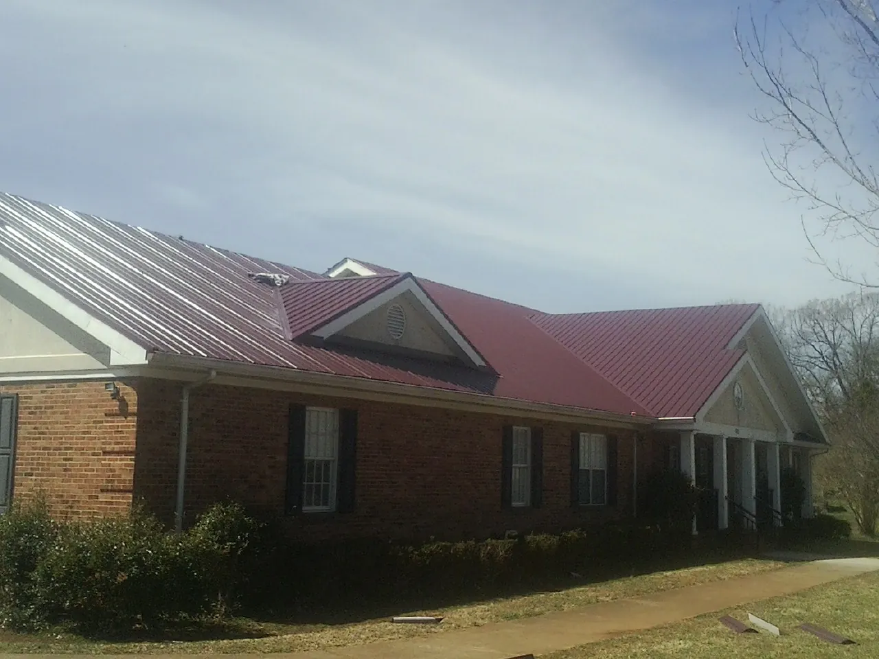 Red metal roof with gabled entries on a long brick building, from a Hail Damage Roof Repair job in San Ysidro