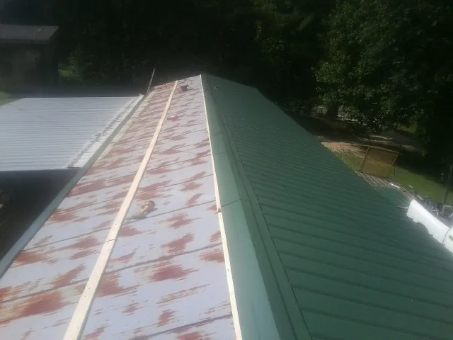 Old rusted panels beside newly installed green metal roofing in San Ysidro
