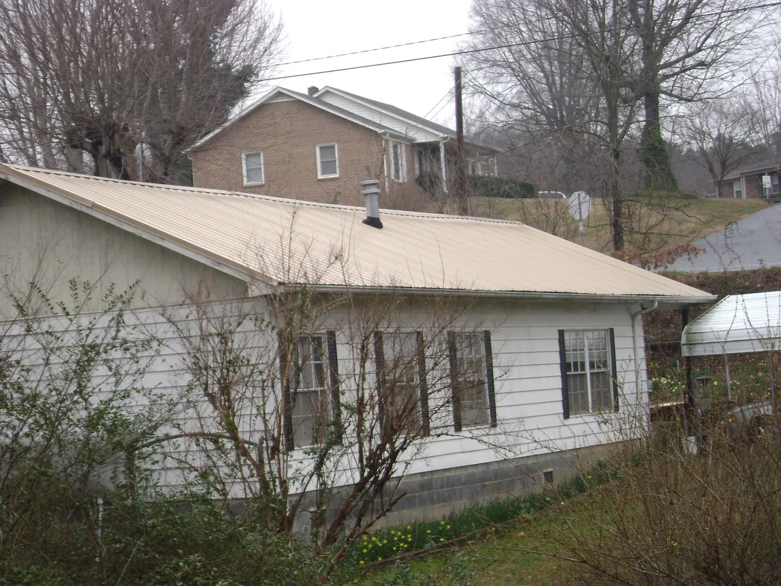 Tan metal roof on a white sided house set into a hillside — Commercial Roofing by Roofing Brothers in San Ysidro